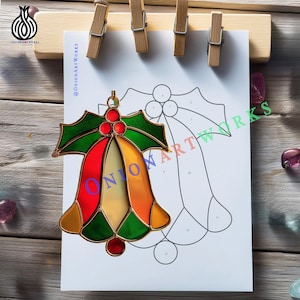 Può includere: Un ornamento a campana natalizia in vetro colorato con pannelli rossi, arancioni, verdi e gialli. L'ornamento è appeso davanti a un disegno del motivo della campana, tenuto da mollette di legno. L'ornamento ha un contorno metallico color oro.