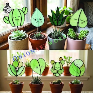 Puede incluir: Una colección de estacas para plantas de vidrio manchado verde con varios diseños de caras, incluyendo un cactus, una gota, una aloe y una hoja. Cada estaca se coloca en una pequeña suculenta en maceta. El texto "ONIONARTWORK" es visible.