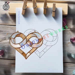 May include: A stained glass heart-shaped ornament with a gold-colored metal frame. The glass has a pearlescent, opalescent appearance. The ornament is displayed on a white paper with a heart outline and the text "ONION ARTWORKS".