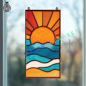 Puede incluir: Panel de vidrieras que representa una puesta de sol sobre el océano. El sol es de color naranja vibrante, con rayos rojos y naranjas. El océano es azul y blanco, con una playa de arena en la parte inferior. El panel está enmarcado en metal oscuro.