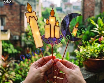 May include: Three stained glass plant stakes featuring a tall cream candle, a cluster of three cream candles in a purple lotus base, and a purple crescent moon with a small cream candle, all attached to thin copper-colored metal rods.