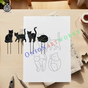 May include: Three black stained glass cat figures with metal stakes stand next to a white paper pattern sheet featuring black line drawings of cats labeled with numbers. The paper includes outlines for multiple cat shapes for glass crafting.