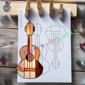 May include: A stained glass guitar with a wooden frame, featuring shades of brown, orange, and cream. The guitar is hanging in front of a drawing of a guitar. The text "@OnionArtWorks" is visible.