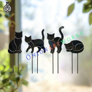 May include: Four black stained glass cat silhouettes, each mounted on two thin metal stakes. The cats are depicted in different poses: sitting, walking, arching their backs, and sleeping. The text ONION ART WORKS is visible in blue and green.