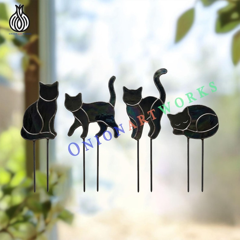 May include: Four black stained glass cat silhouettes, each mounted on two thin metal stakes. The cats are depicted in different poses: sitting, walking, arching their backs, and sleeping. The text ONION ART WORKS is visible in blue and green.