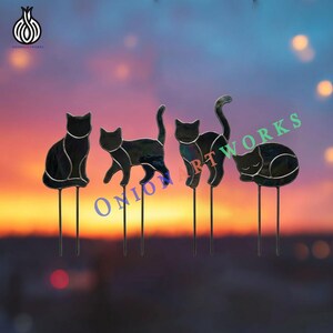 May include: Four black stained glass cat silhouettes mounted on metal stakes. Each cat figure features distinct poses: sitting, walking, arching its back, and sleeping. The glass has a dark, iridescent finish with visible silver solder lines.