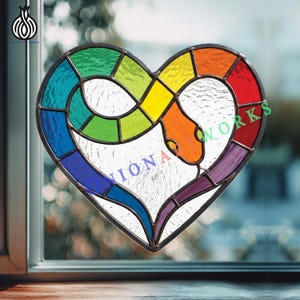 Op de afbeelding: Een gebrandschilderd glazen hart met een regenboogkleurenschema en een slangmotief. Het hart is verdeeld in secties van rood, oranje, geel, groen, blauw en paars. De tekst "IONA WORKS" is zichtbaar.