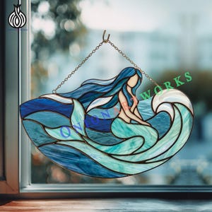 May include: A stained glass suncatcher featuring a mermaid with flowing blue hair and a teal tail, positioned amidst swirling ocean waves in shades of deep blue, light blue, and white. The piece is suspended by a metal chain for window display.