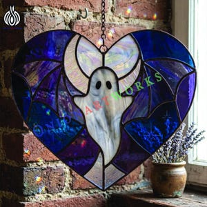 May include: A heart-shaped stained glass suncatcher featuring a white ghost with black eyes centered against a dark blue and purple background. The piece includes iridescent glass accents and a metal chain for hanging. The text ONION ART WORKS is visible.