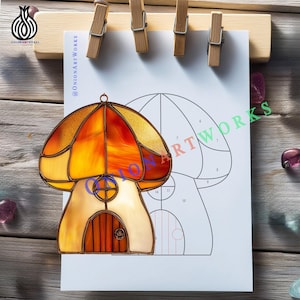 May include: A stained glass mushroom house with a warm color palette of orange, yellow, and cream. The mushroom house is hanging in front of a drawing of a mushroom house. The image is held by wooden clothespins.