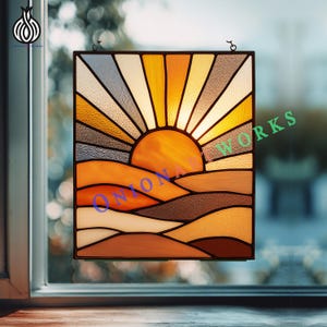 May include: Stained glass panel showing a sunset over rolling hills. The artwork uses orange, yellow, brown, and white. The sun's rays burst from behind a large orange sun. The panel is framed in black and hangs in front of a window. The word "ONIONA" is visible.