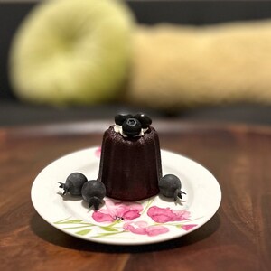 May include: A dark chocolate cake with a white frosting and blueberries on top, served on a white plate with a floral design.