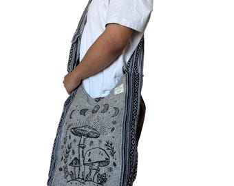 May include: A gray shoulder bag with a black and white mushroom and moon graphic. The bag has a wide strap and a patterned border. The bag is made of a woven fabric.
