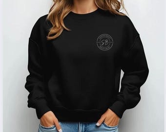 May include: Black crew neck sweatshirt with the text "SLEEPING BEAUTY BEAUTY SALON" in a circular design on the upper left chest. The sweatshirt is a solid black color and is made of a soft material.