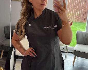 May include: A woman wearing a black uniform with the text "GALJ MAJ" in pink. She is holding a phone with a pink and white marble case.