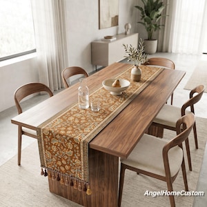 May include: A wooden dining table set with six chairs, a patterned table runner, and decorative items. The table runner is brown with a floral design and tassels. A glass bottle, a bowl with a pear, and a vase with olive branches are on the table.