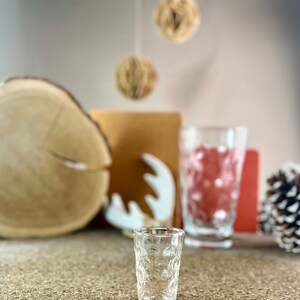 Peut inclure: Un verre &agrave; shot en verre transparent avec un motif textur&eacute; en forme de bulles. Le verre est pos&eacute; sur une surface brune.