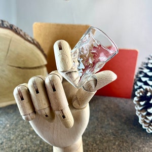 Peut inclure: Un verre &agrave; shot en verre transparent avec une surface textur&eacute;e. Le verre est tenu par une main en bois.