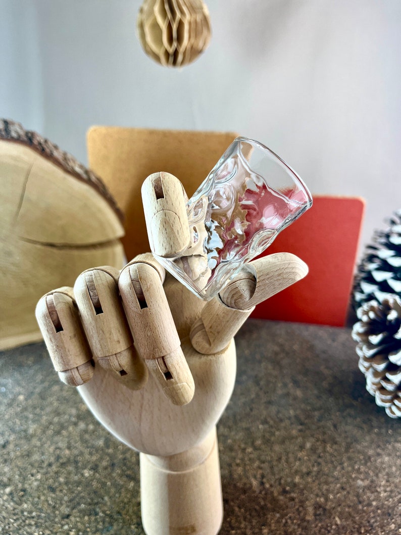 Peut inclure: Un verre &agrave; shot en verre transparent avec une surface textur&eacute;e. Le verre est tenu par une main en bois.