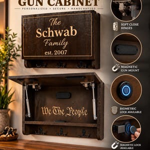 May include: A dark wood wall-mounted cabinet featuring the text The Schwab Family est. 2007 on the front. The interior displays the text We The People, soft close hinges, a magnetic gun mount, and a biometric lock with a blue light indicator.