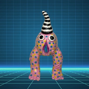 Pode incluir: Uma escultura de cerâmica extravagante de uma criatura com um corpo rosa adornado com bolinhas azuis e amarelas. Possui olhos grandes e expressivos, um chapéu listrado em preto e branco e uma boca azul e rosa. A escultura repousa sobre duas pernas arqueadas.