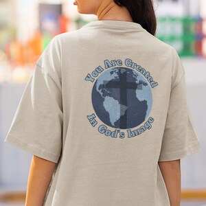 May include: A beige t-shirt with a blue and white graphic of a globe with a cross on it. The text "You Are Created In God's Image" surrounds the globe.