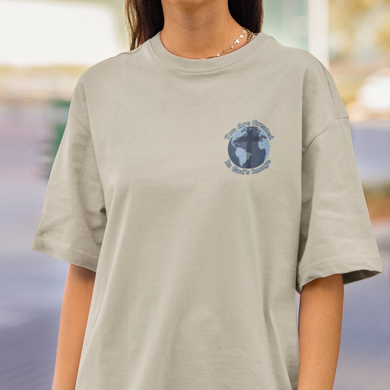 May include: A light gray t-shirt with a blue and white graphic of a globe with a cross on it. The graphic says "You are Created in God's Image".
