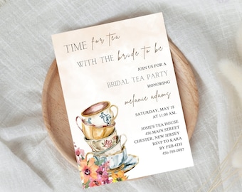 May include: A bridal tea party invitation with a watercolor illustration of stacked teacups and flowers. The invitation is for Melanie Adams and includes the date, time, and location of the event. RSVP information is also included.