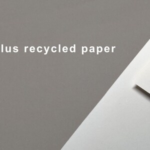 May include: A close-up of a white sheet of paper with the text "Cyclus recycled paper" printed on it. The paper is folded in half and the top layer is slightly lifted to reveal the white paper underneath. The background is a light gray color.