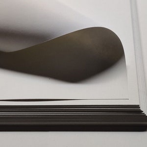 May include: A stack of white cardstock paper with one sheet curled up at the edge. The paper is smooth and has a slight sheen.