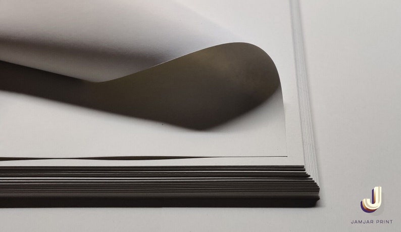 May include: A stack of white cardstock paper with one sheet curled up at the edge. The paper is smooth and has a slight sheen.