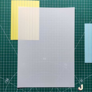 May include: A white sheet of paper with a grid pattern and faint markings for angles. The paper is placed on a green cutting mat with white markings.