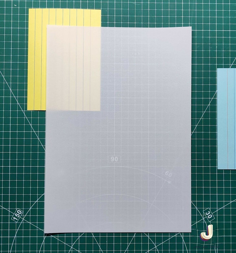 May include: A white sheet of paper with a grid pattern and faint markings for angles. The paper is placed on a green cutting mat with white markings.