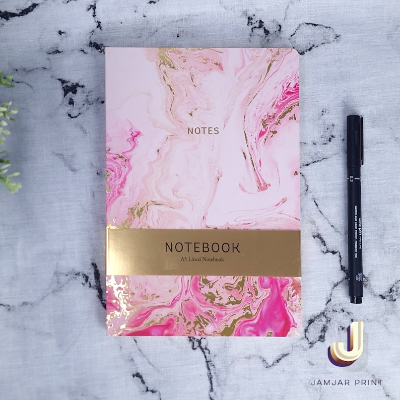 Może przedstawiać: R&oacute;żowy i złoty marmurowy notes z napisem "NOTES" i "NOTEBOOK A5 Lined Notebook" na okładce.