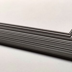 May include: A stack of white cardstock paper, showing the edge of the stack. The paper is smooth and has a slight sheen.