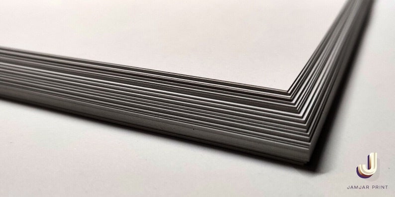 May include: A stack of white cardstock paper, showing the edge of the stack. The paper is smooth and has a slight sheen.