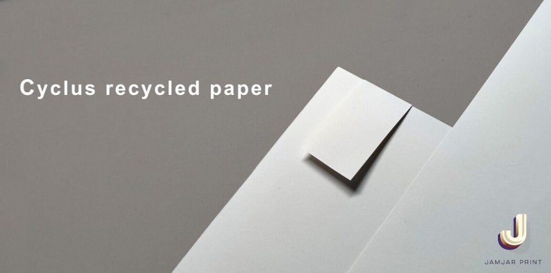 May include: A close-up of a white sheet of paper with the text "Cyclus recycled paper" printed on it. The paper is folded in half and the top layer is slightly lifted to reveal the white paper underneath. The background is a light gray color.