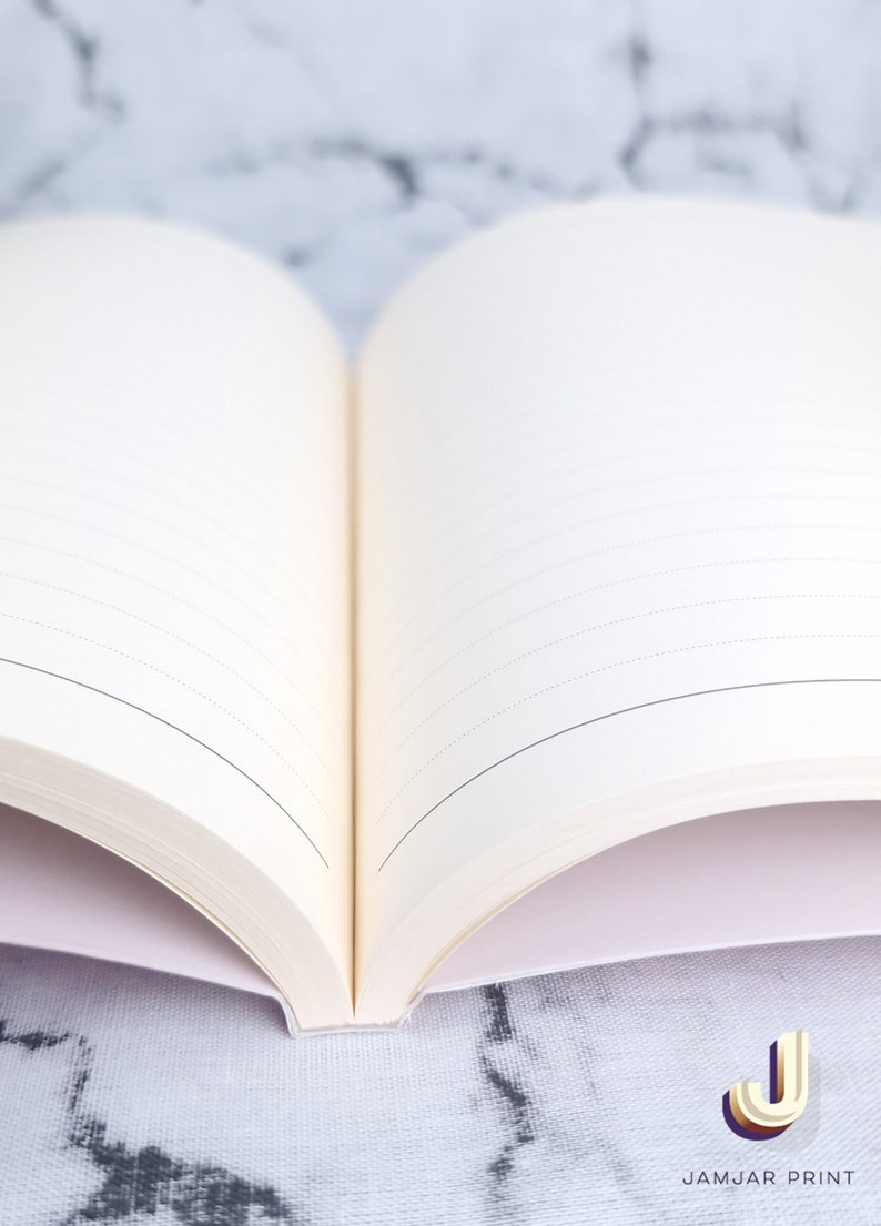 Może przedstawiać: Otwarty pusty notes z liniowanymi stronami, leżący na białym marmurowym blacie. Notes ma białą okładkę i biały grzbiet.