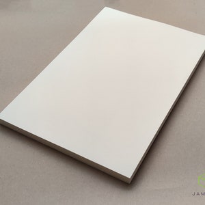 K&ouml;nnte beinhalten: Ein leeres, cremefarbenes Blatt Papier. Das Papier ist glatt und hat einen leichten Glanz.
