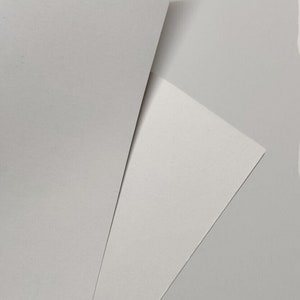 May include: Two sheets of white paper, one on top of the other, with the top sheet folded over to create a triangular shape. The bottom sheet is slightly visible underneath. The image has a white background and the text "JAMJAR PRINT" in the bottom right corner.
