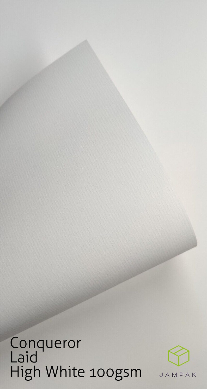 K&ouml;nnte beinhalten: Nahaufnahme eines wei&szlig;en, strukturierten Papierblattes. Das Papier ist mit "Conqueror Laid High White 100gsm" beschriftet und hat eine subtile, gepr&auml;gte Textur. Das Papier ist &uuml;ber sich selbst gefaltet und zeigt die wei&szlig;e Unterseite.