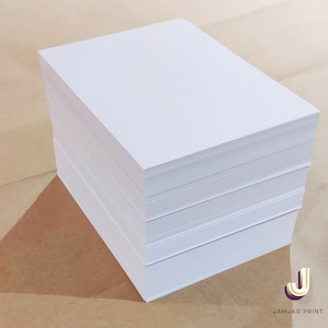 May include: A stack of white paper, probably printer paper, on a brown surface. The paper is neatly stacked and looks new.