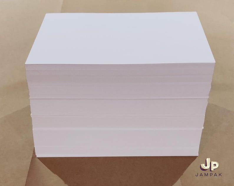 May include: A stack of white rectangular paper sheets, likely for printing or writing. The paper is neatly stacked, showing clean edges and a smooth surface. The image is taken from a slightly elevated angle, highlighting the stack's thickness and the crisp white color of the paper.