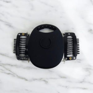 以下が含まれることがあります： 中央に丸い黒いシリコン製の部品が付いた黒いヘアクリップ。シリコン製の部品の中央には小さな丸い穴があります。