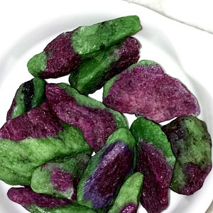 Puede incluir: Una colección de piedras preciosas verdes y moradas, con una textura rugosa y natural. Las piedras están dispuestas sobre una superficie blanca.