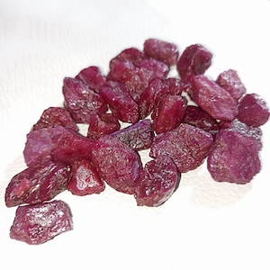 May include: A collection of loose, raw ruby gemstones. The rubies are a deep, rich red colour and have a variety of shapes and sizes.
