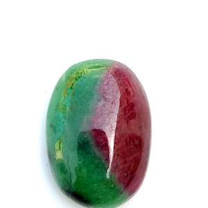 Puede incluir: Una piedra preciosa pulida de forma ovalada con una superficie lisa y un patrón de color distintivo en verde vibrante y rojo magenta intenso. La piedra muestra un acabado brillante con variaciones naturales en la distribución del color.