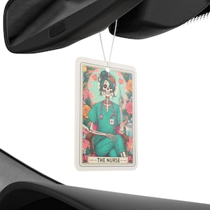 May include: A white car air freshener with a colorful illustration of a skeleton wearing a green nurse's uniform and holding a syringe. The text "THE NURSE" is printed below the image.
