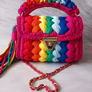 May include: A rainbow crocheted handbag with a gold chain strap and a gold clasp. The bag has a tassel made of rainbow colored yarn.