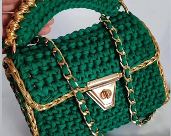 May include: A green crocheted handbag with a gold chain strap and a gold clasp. The bag has a top handle and a flap closure.